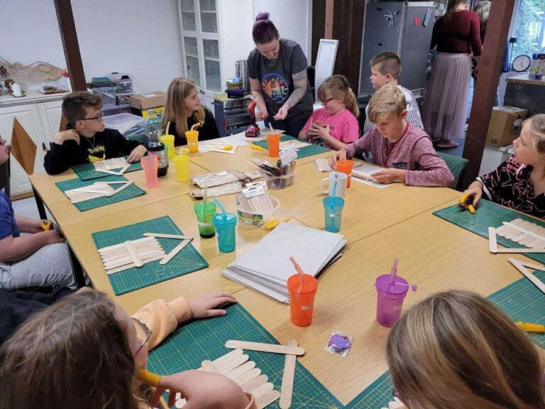 Kinder und Betreuerinnen basteln gemeinsam an langen Tischen im Gemeinschaftsraum