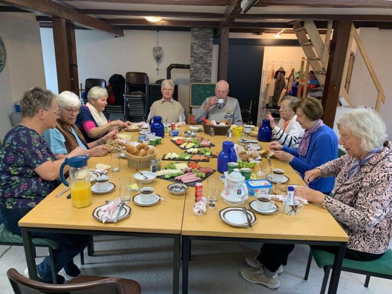 Seniorinnen und Senioren beim gemeinsamen Frühstück an einer langen Tafel im Haus Kunterbunt