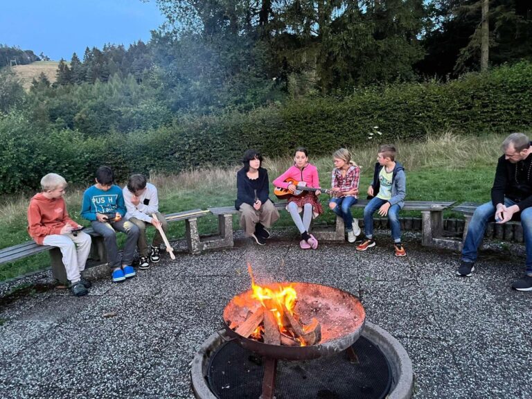 Gruppe sitzt abends gemeinsam um ein Lagerfeuer
